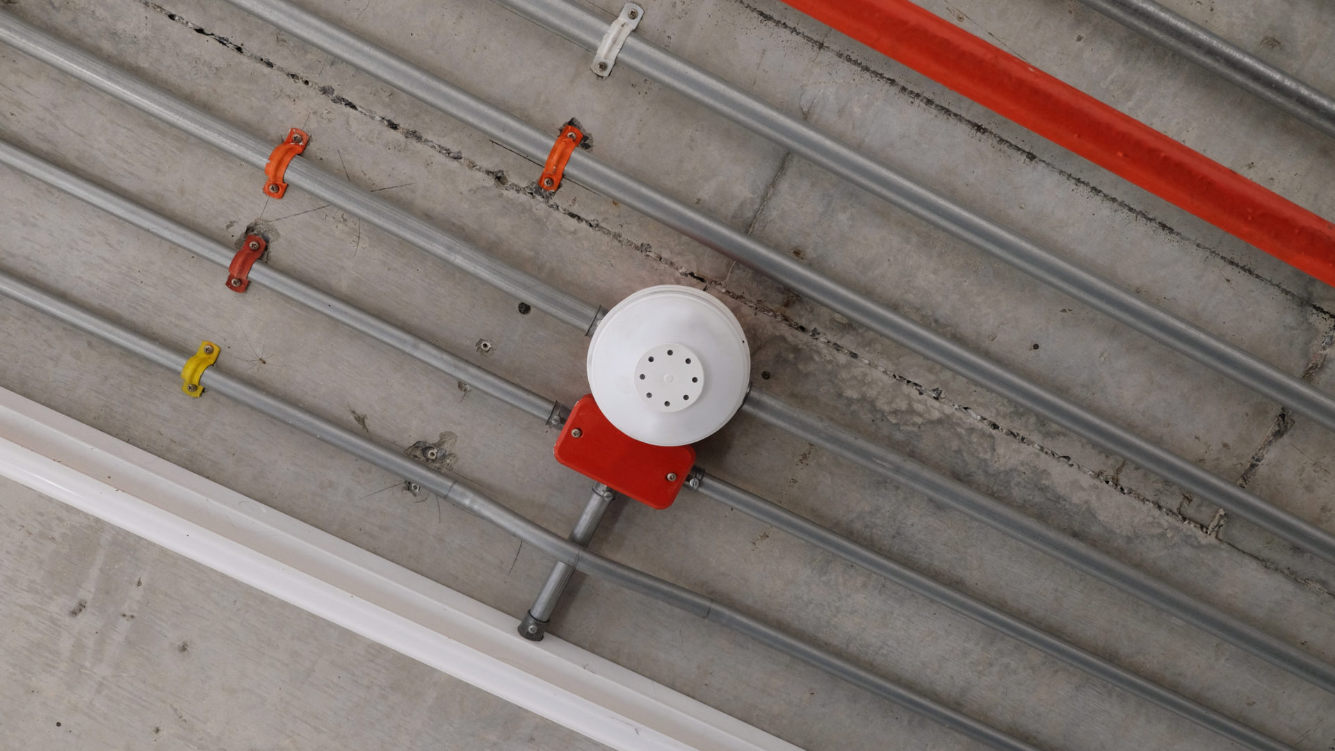 White smoke detector installed on the ceiling at car parking area with pipeline of electrical wiring